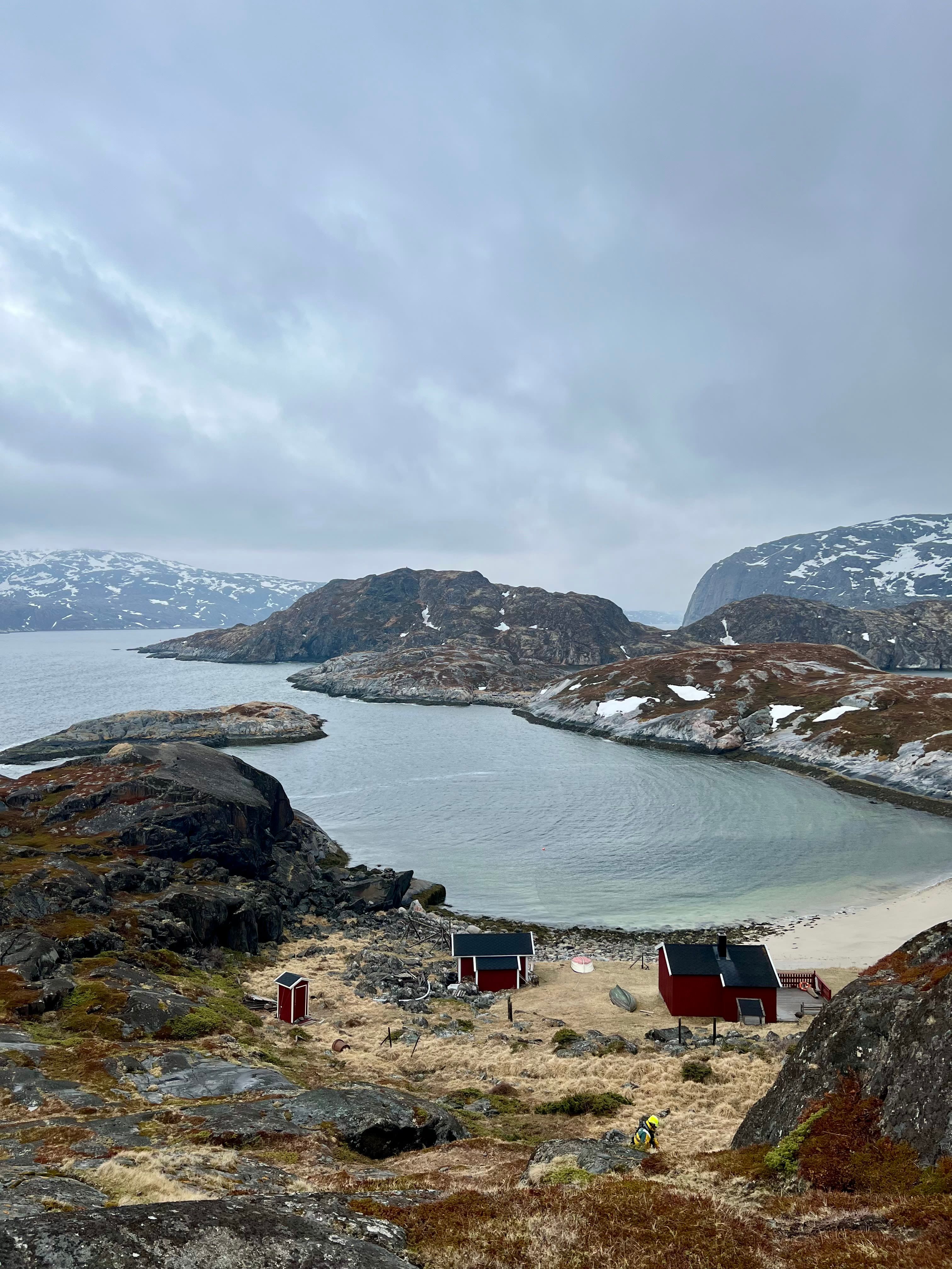 Scenic Arctic fjord with red cabins and a secluded cove along the Arctic Rappelling Route in Northern Norway.