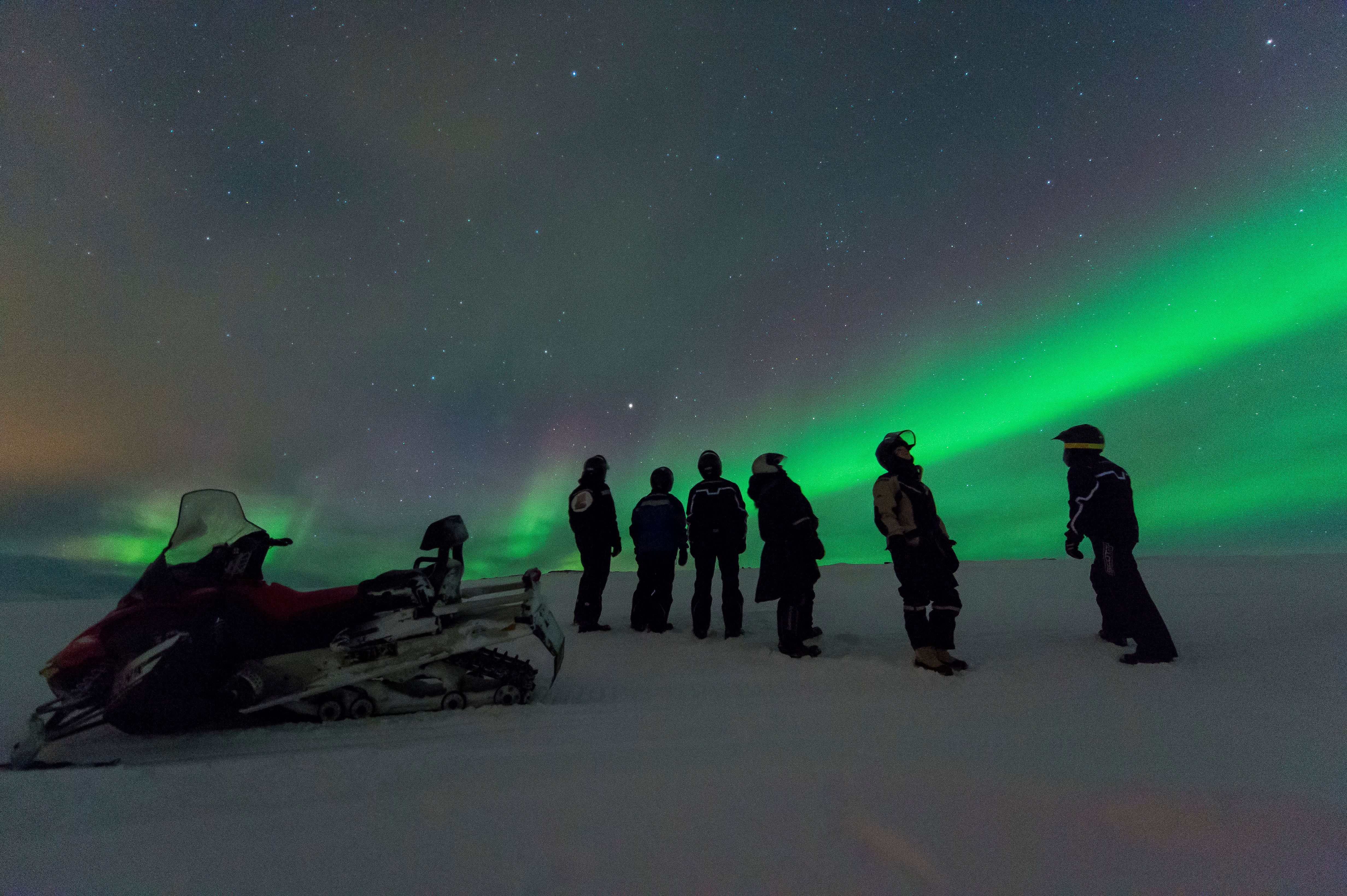 Group of people looking at the northern lights on a snowmobile trip