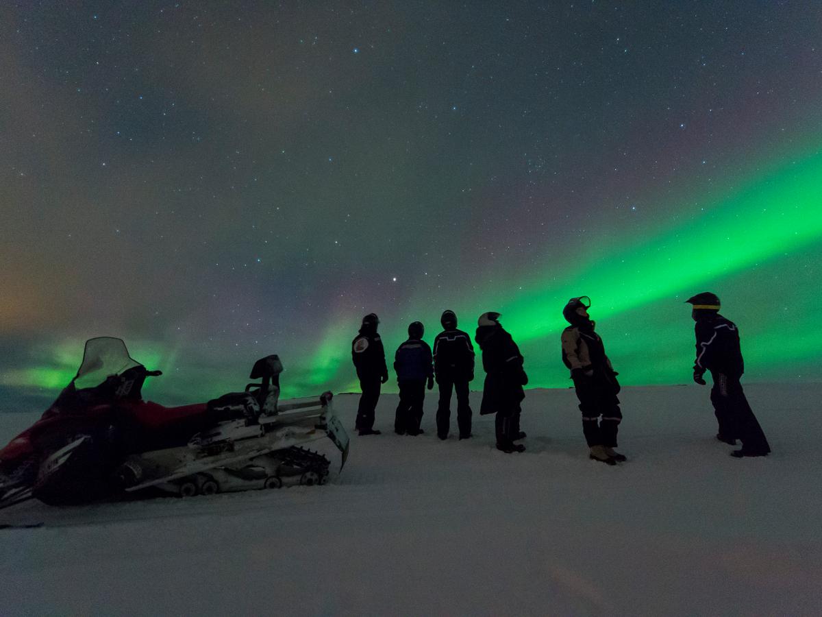 Guests beside snowmobiles under the Northern Lights during a polar night excursion in Arctic Norway.