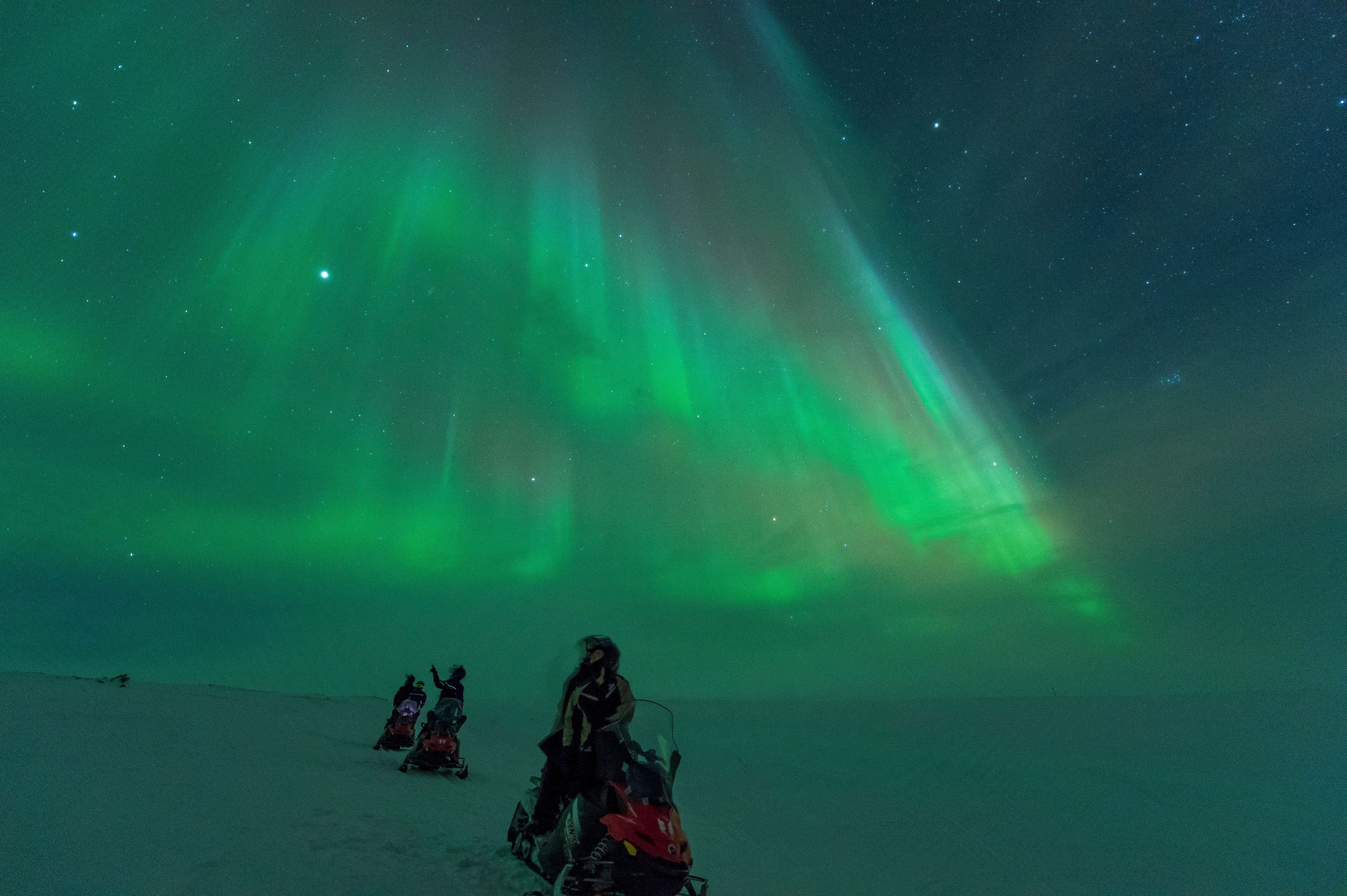Turist som fotograferar norrskenet bredvid två snöskotrar