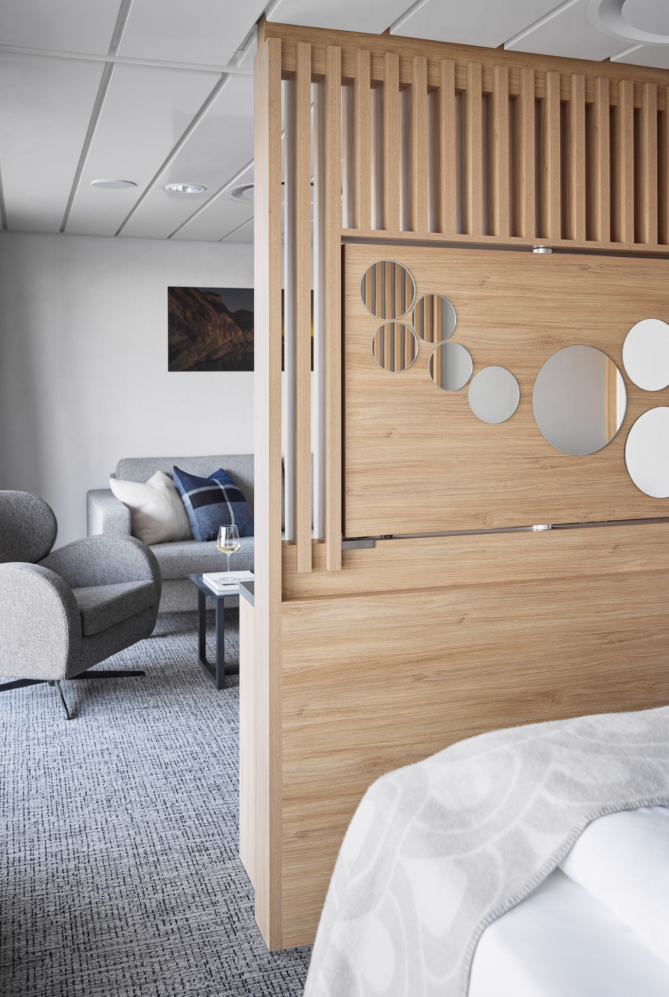 Wooden room divider with decorative circular mirrors separating the bedroom from the suite's living area with a sofa and armchair.