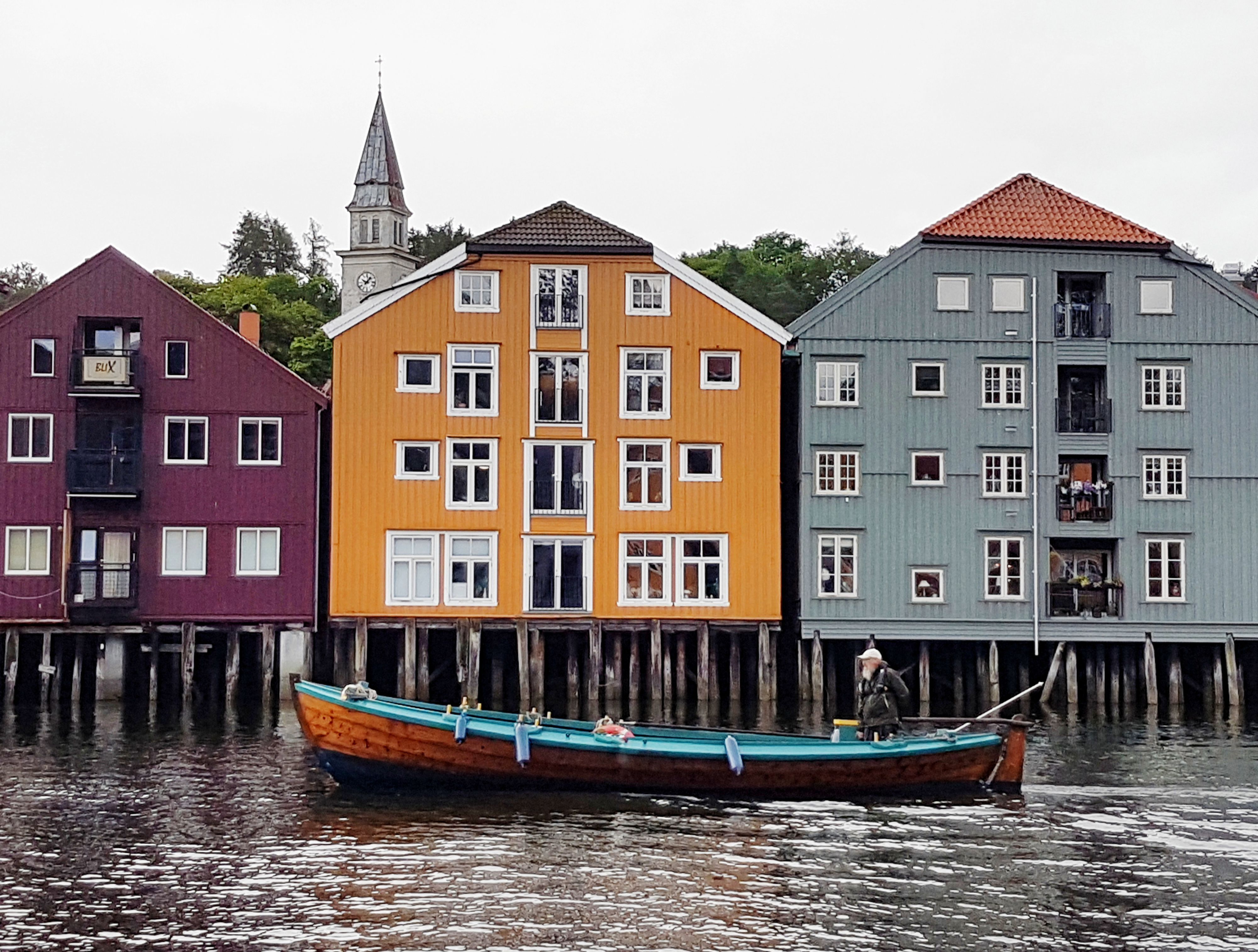 Mann rudert in einem traditionellen Holzboot an bunten Pfahlkais am Fluss Nidelva in Trondheim, Norwegen, vorbei