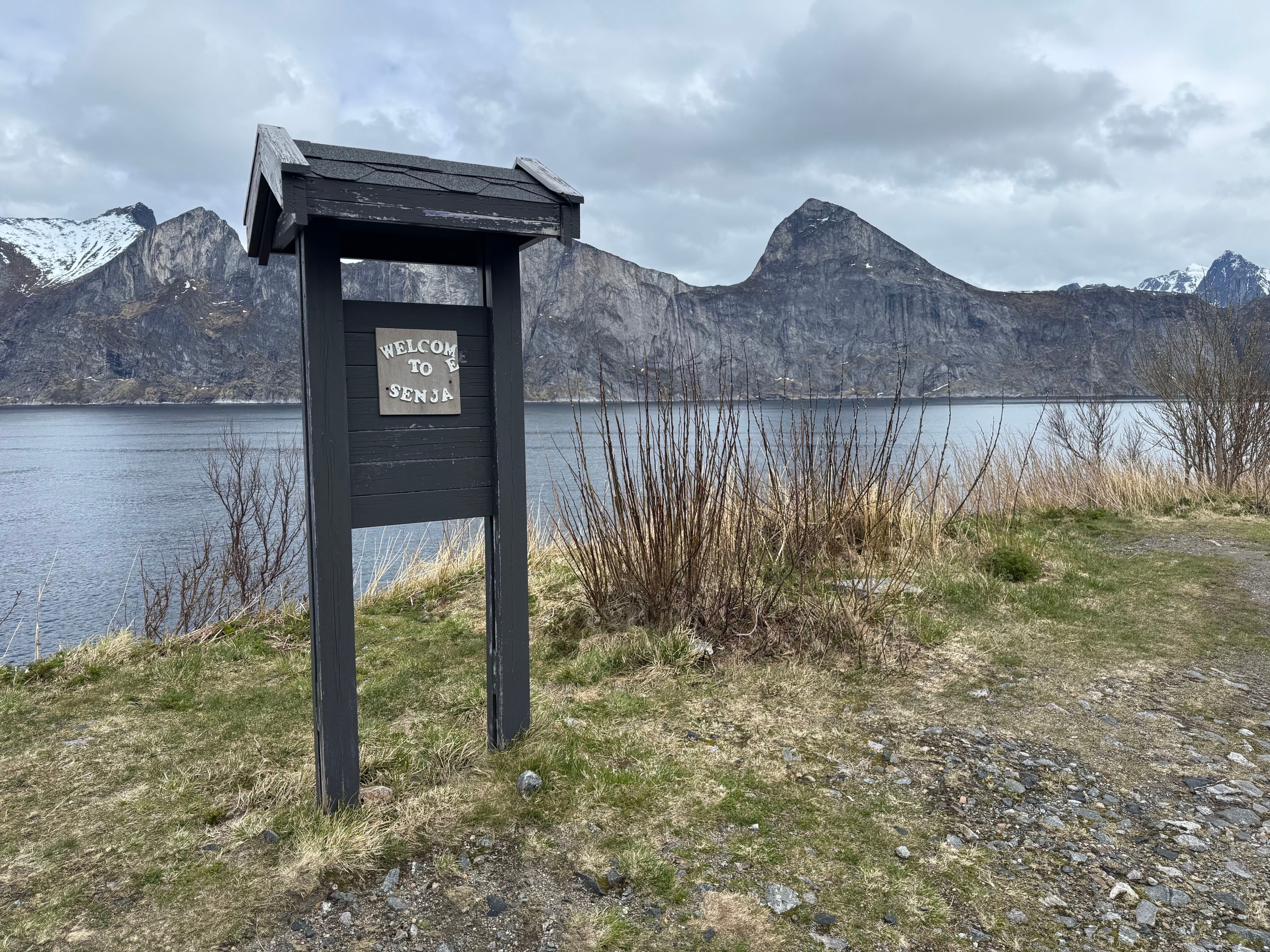 Velkommen til Senja-skiltet med utsikt over en stille fjord og dramatiske fjelltopper, som markerer starten på Nasjonal turistveg i Nord-Norge.