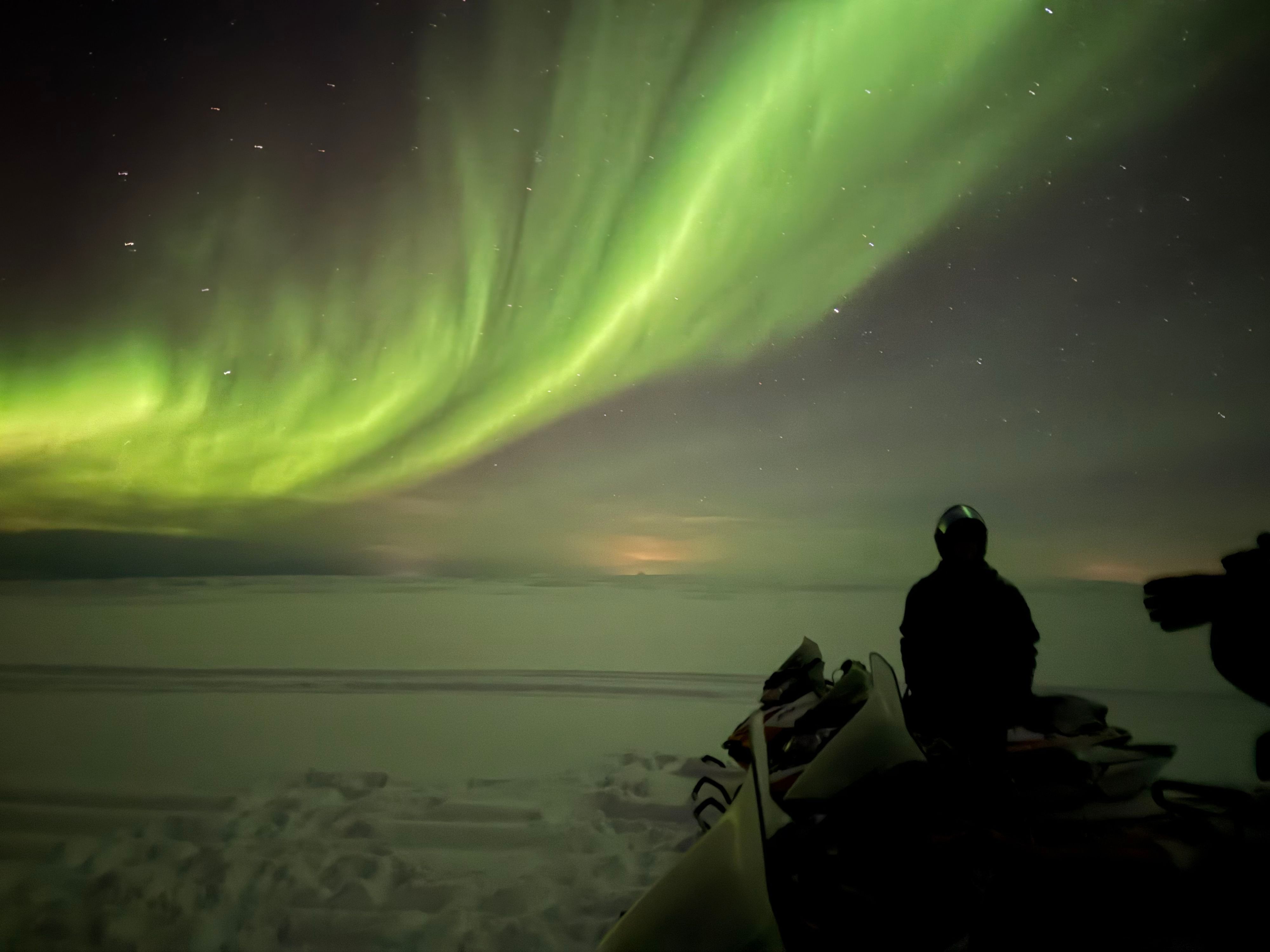 Snowmobiles beneath the Northern Lights during a night tour from Kjøllefjord.