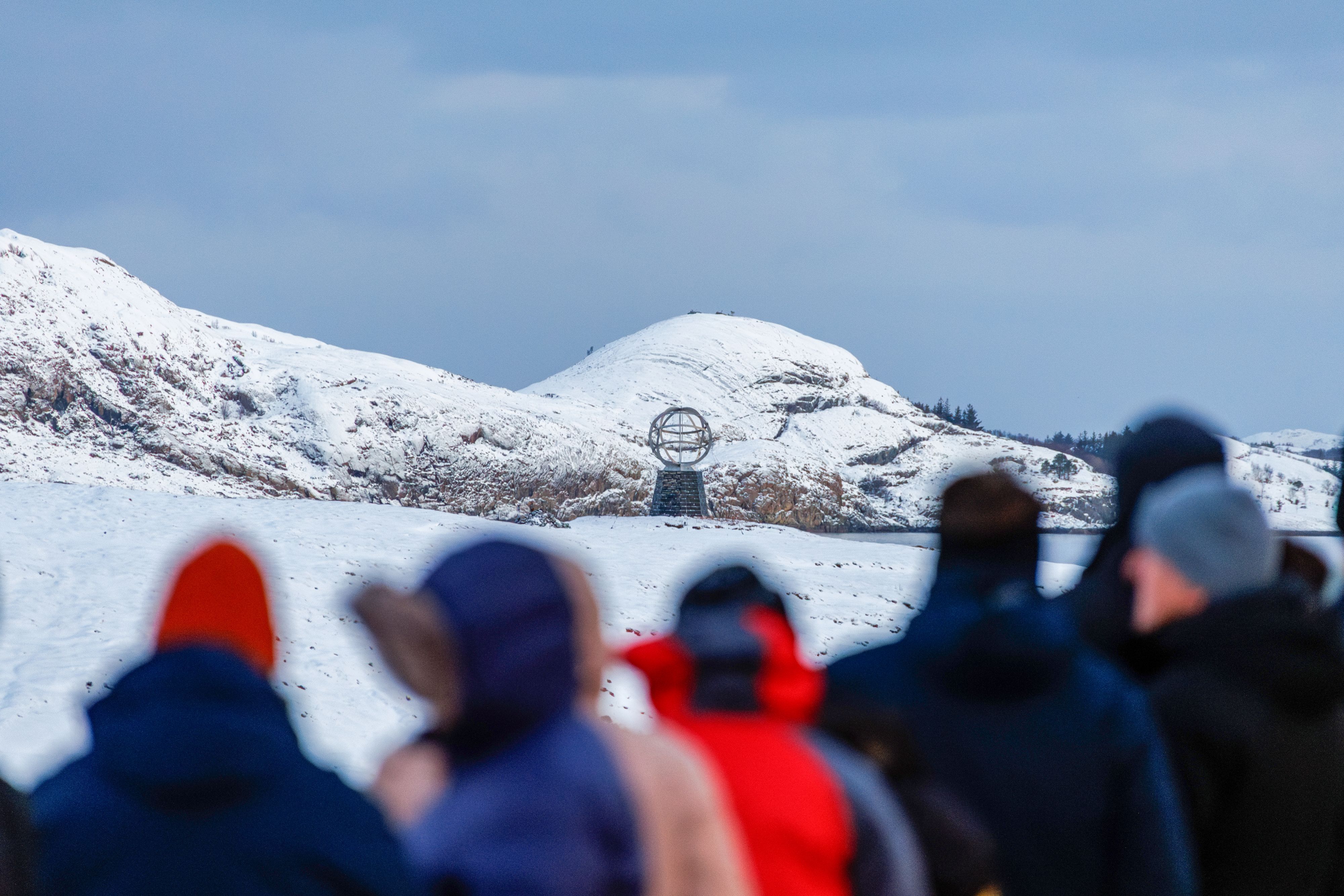 Guests on deck watching the Arctic Circle globe monument on a snow-covered shore