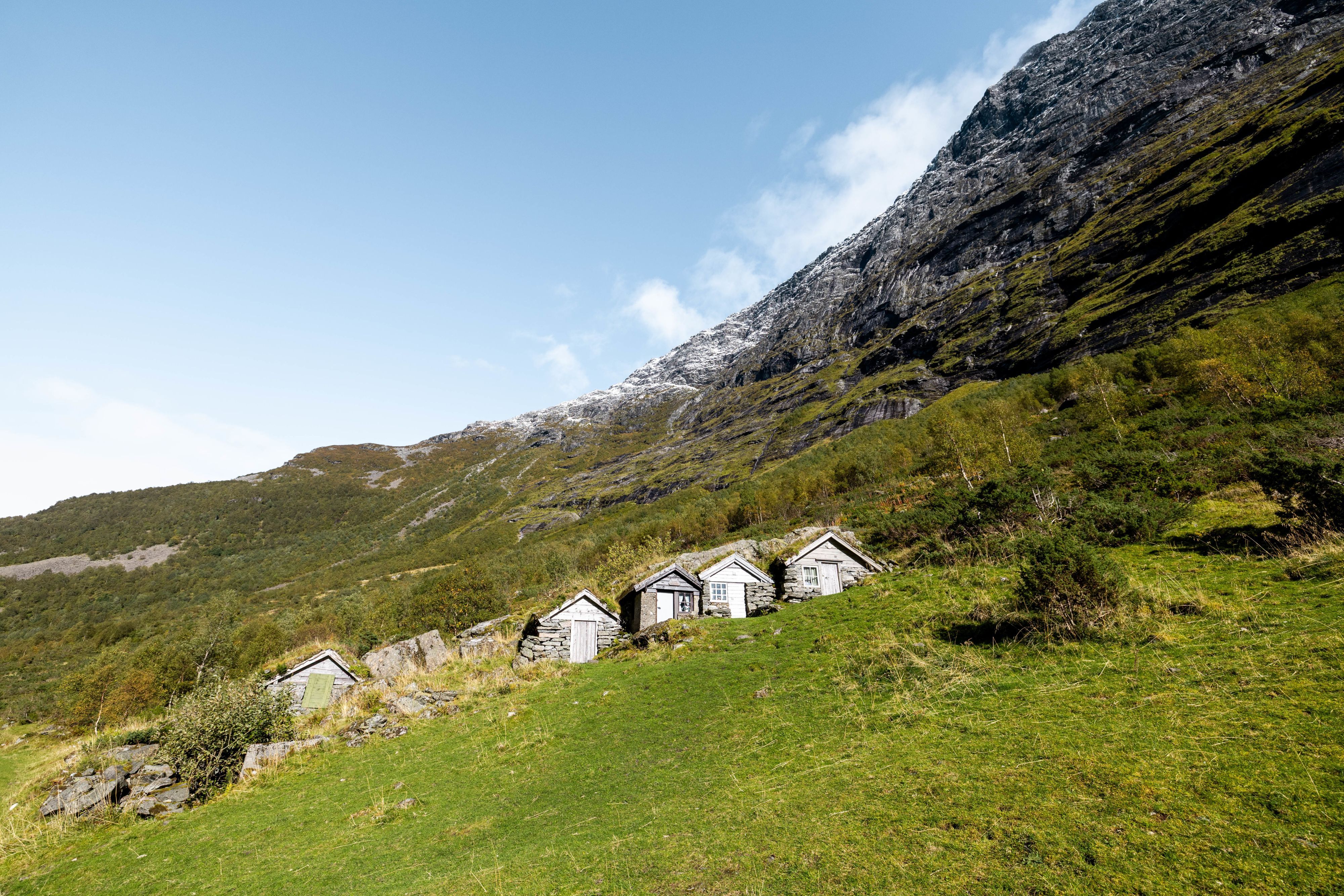 Cluster of old turf-roof stone cabins on a green mountainside in rural Norway