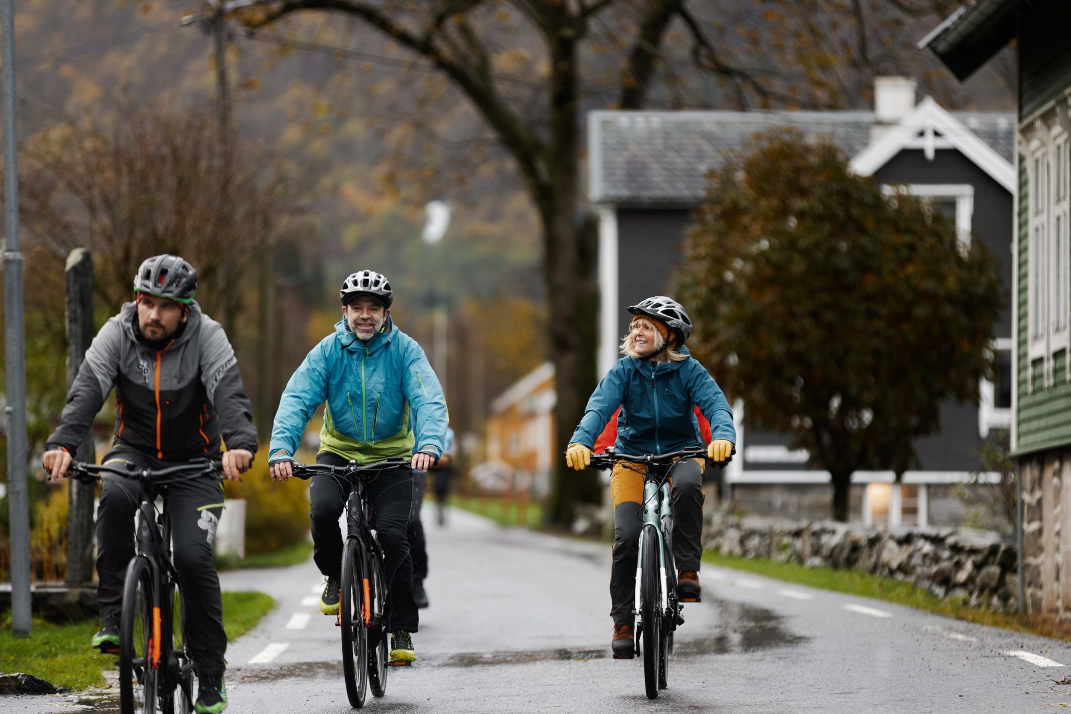 Cyclists on an electric bike tour riding through a quiet village street in autumn, rural Norway