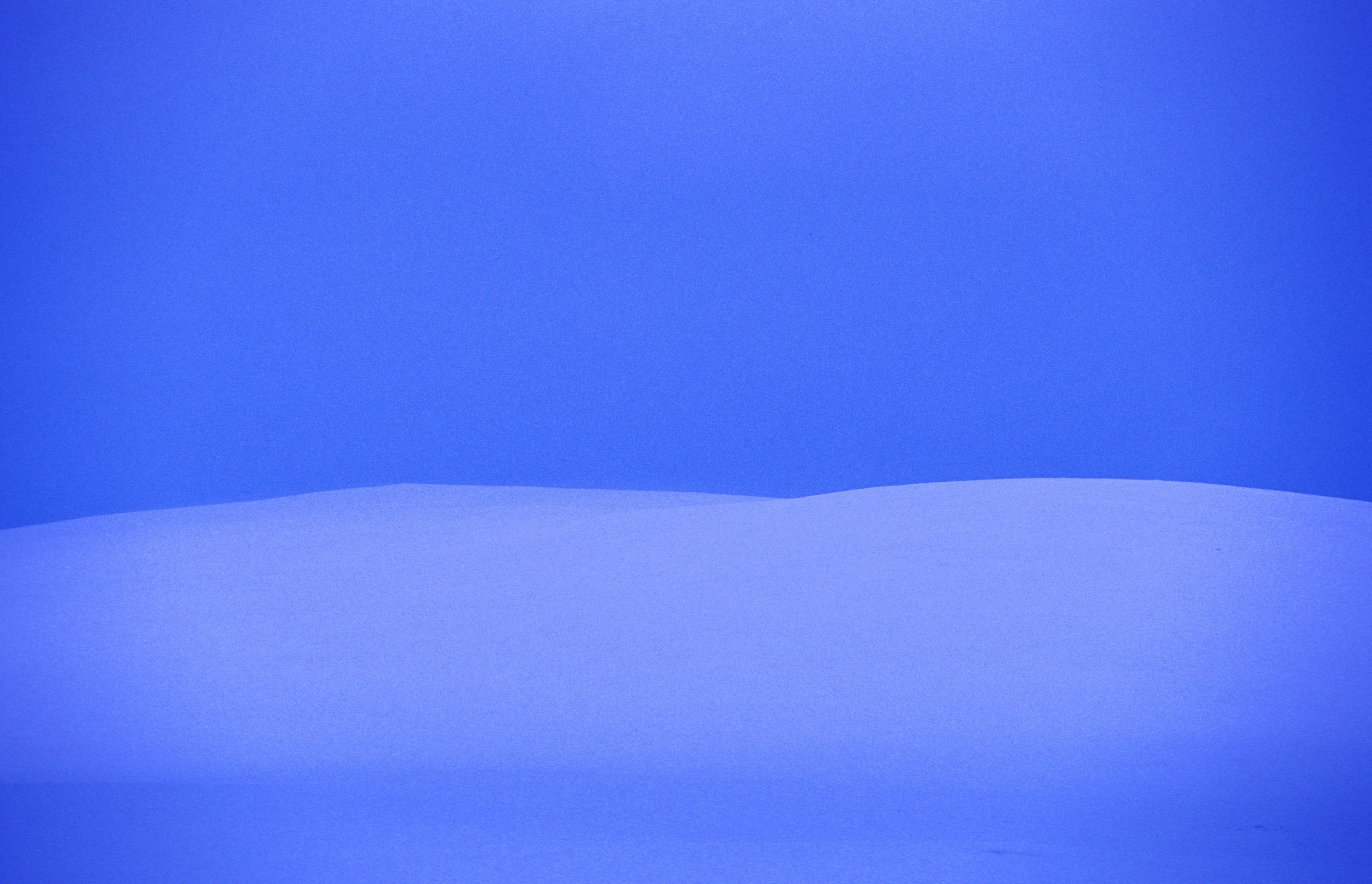 Minimalist Arctic winter landscape with rolling snow-covered hills beneath a deep blue sky.