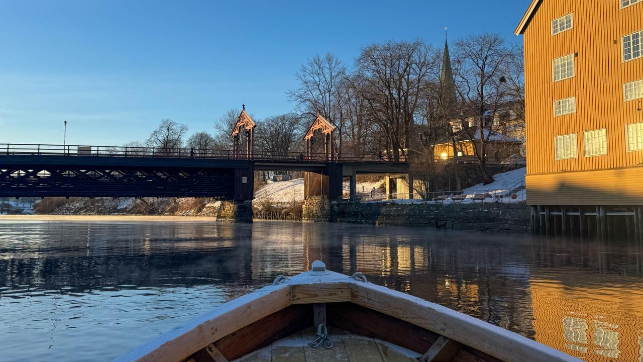 Blick von einem Boot auf die Alte Stadtbrücke und einen gelben Kai an einem frostigen Wintermorgen in Trondheim, Norwegen