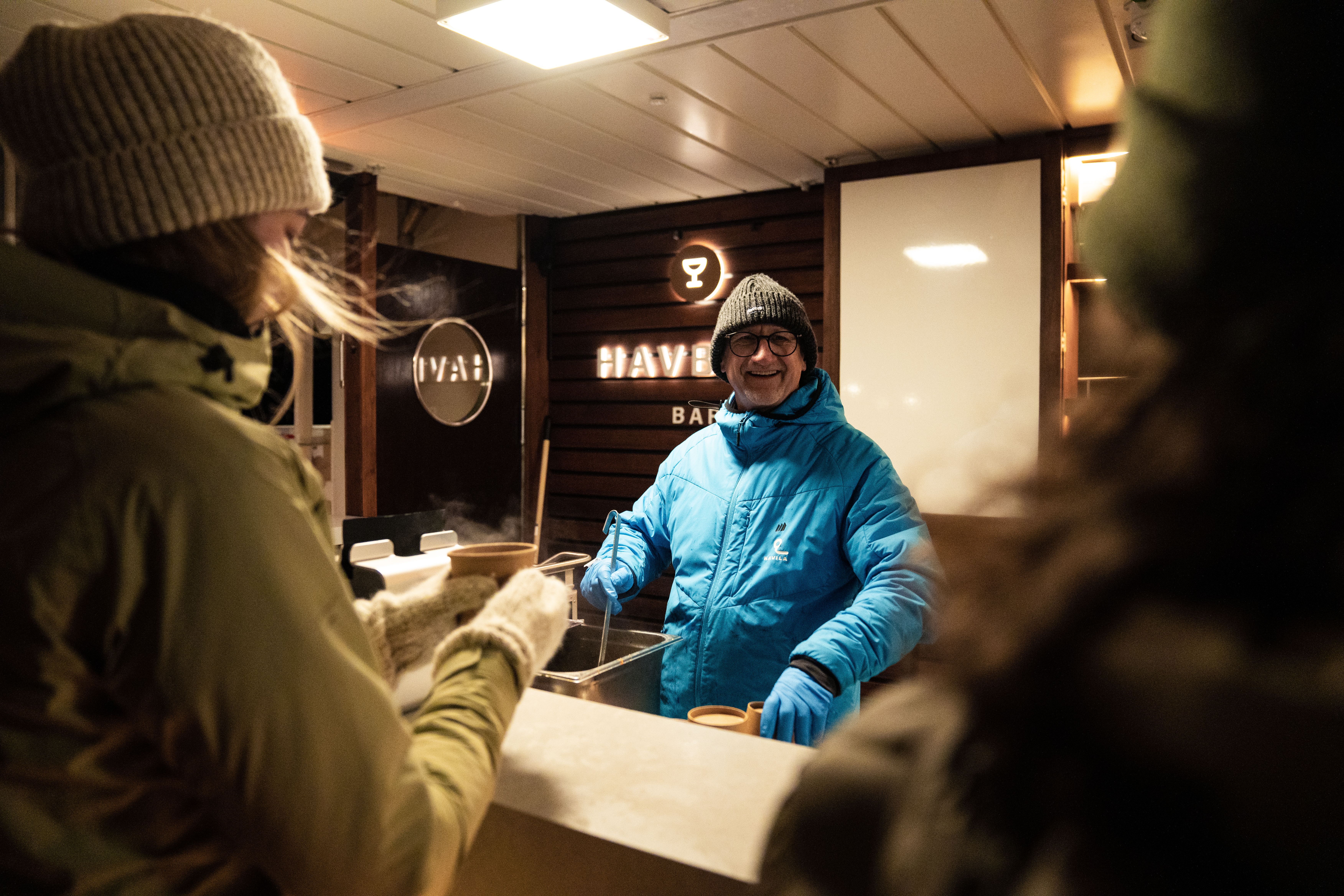 Et besetningsmedlem serverer varm mat til gjester fra baren på utedekket om kvelden