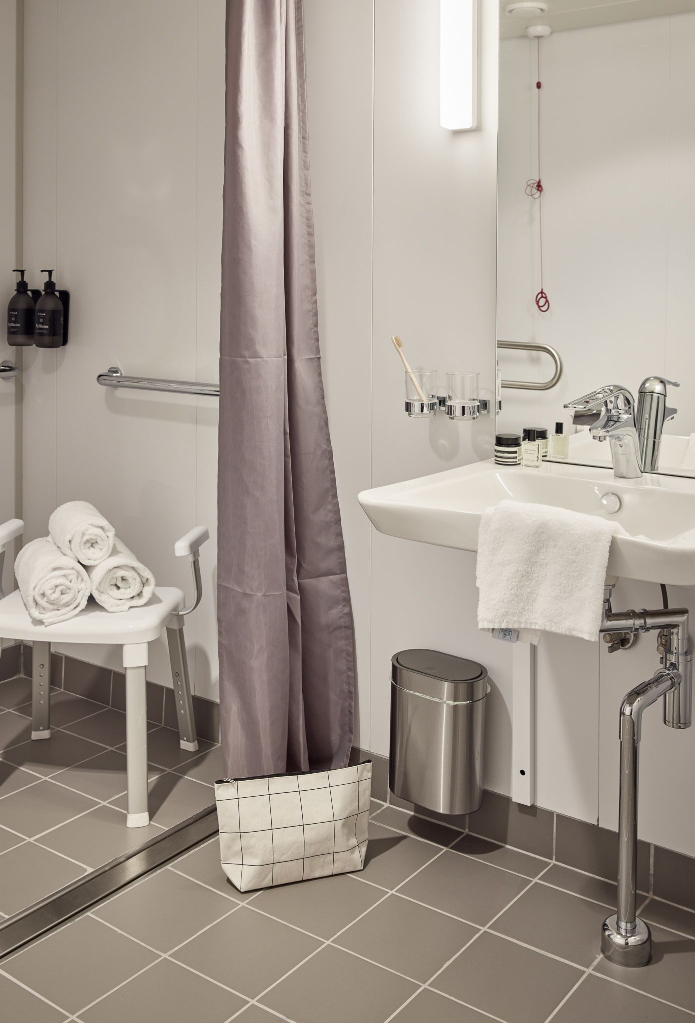 Barrierefreies Kreuzfahrtkabinen-Badezimmer mit begehbarer Dusche, Haltegriffen, barrierefreiem Waschbecken, Duschstuhl und modernen Annehmlichkeiten.