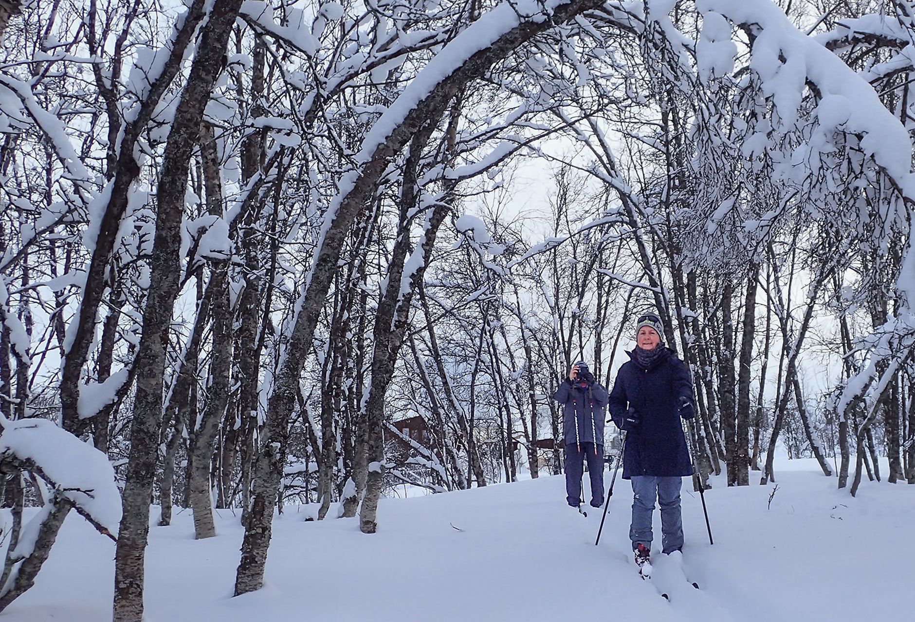 To gjester som øver på klassisk langrenn i preparerte løyper nær Tromsø under en nybegynnertime, omgitt av urørt snø og fredfull arktisk skog.