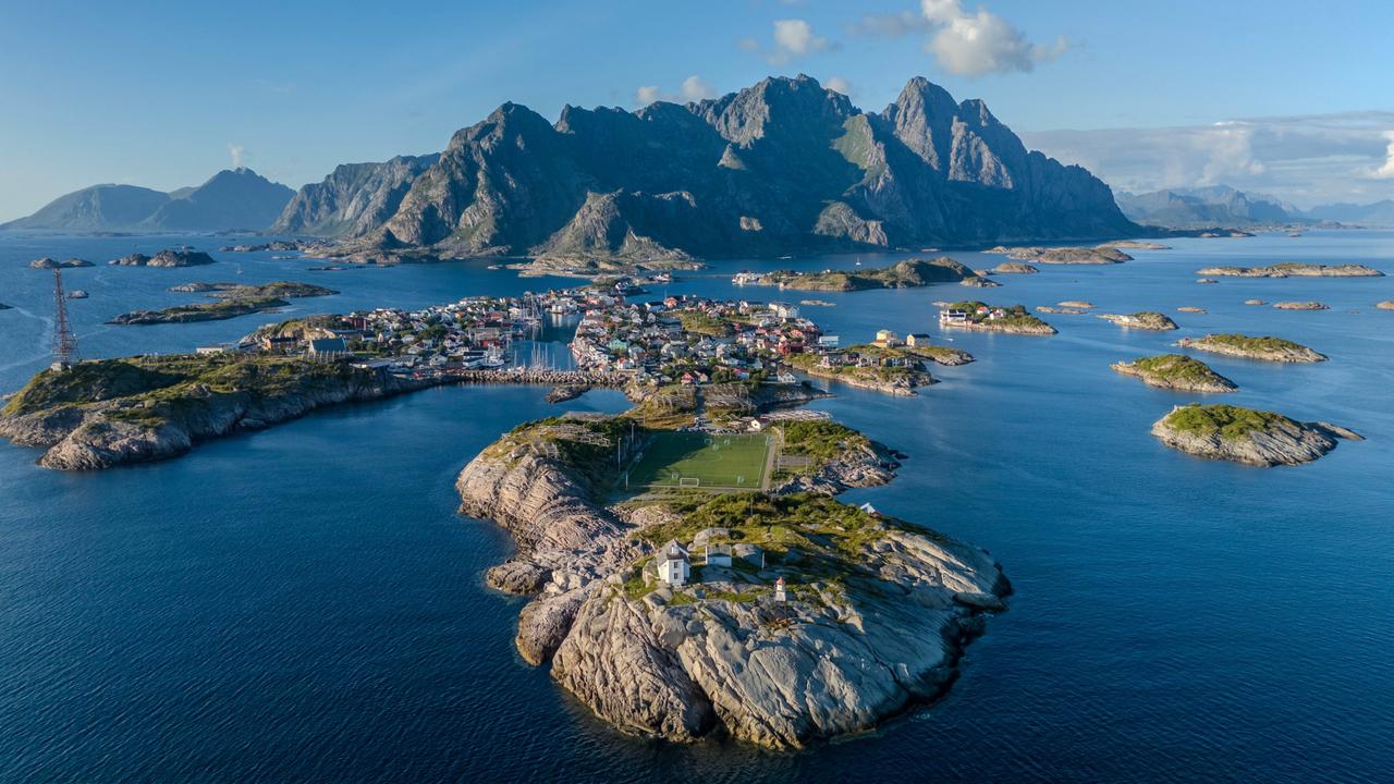 Flygvy över Henningsvær i Lofoten, omgivet av dramatiska berg och Norska havet.
