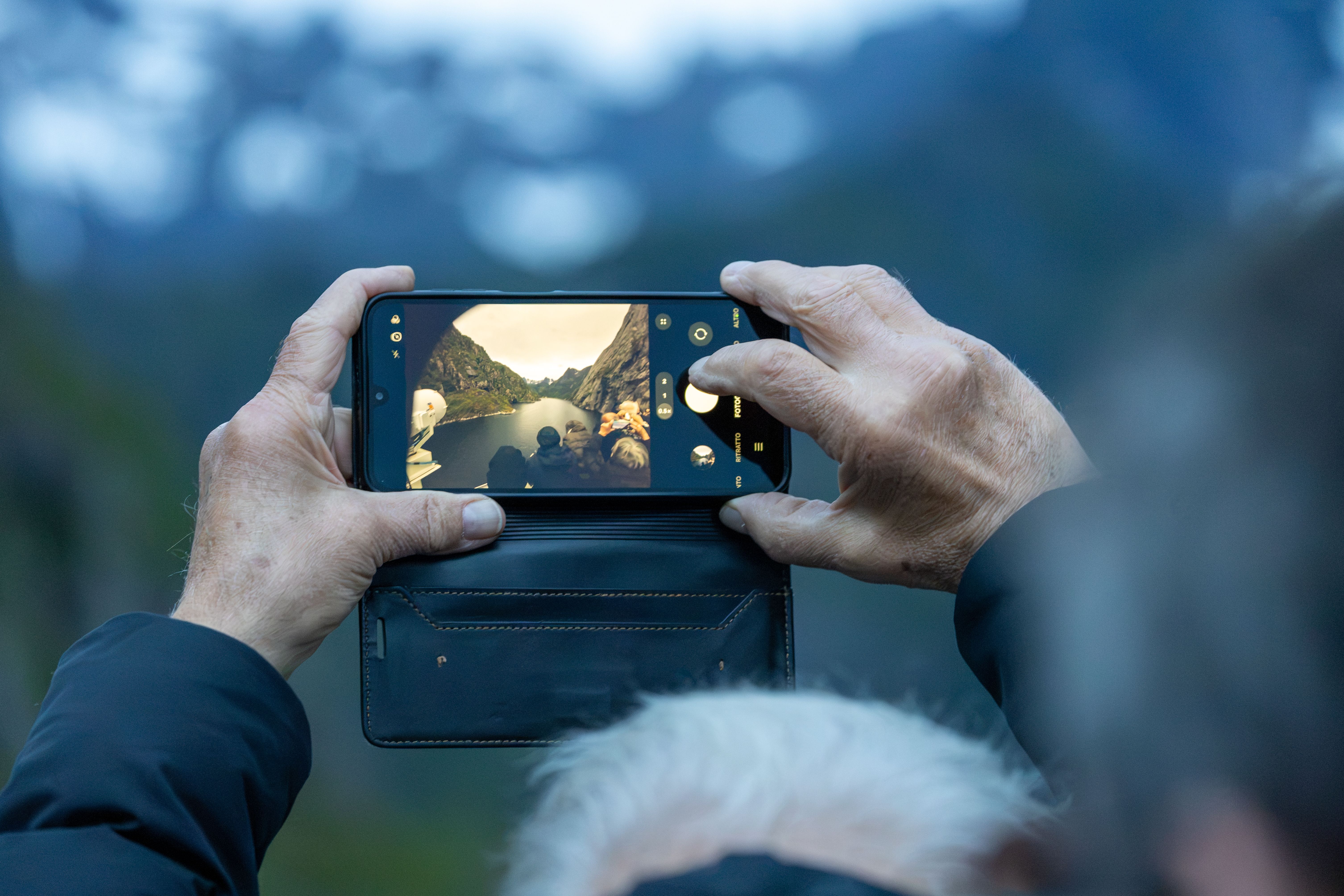 Gjest som holder opp en telefon for å fotografere fjorden og fjellene foran seg