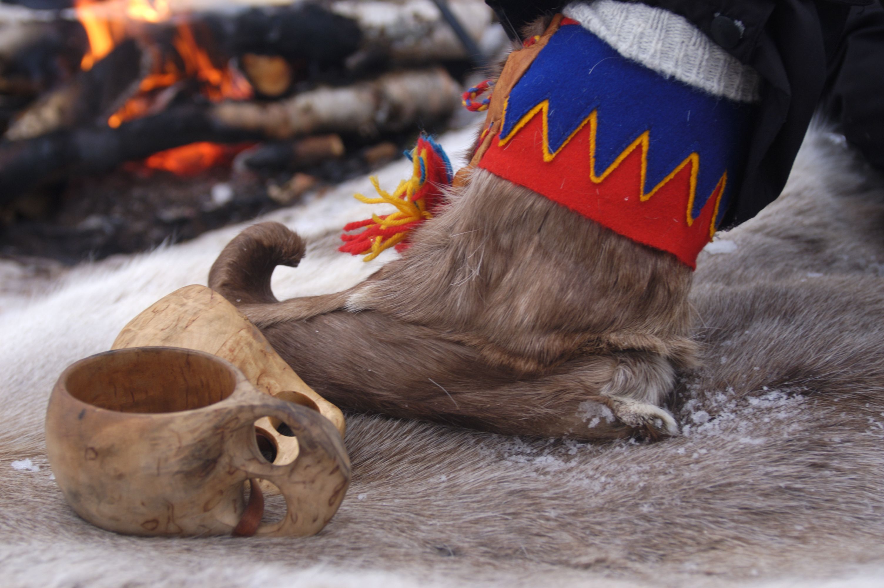 Traditionelle samische Kleidung und Handwerkskunst neben einem winterlichen Lagerfeuer.