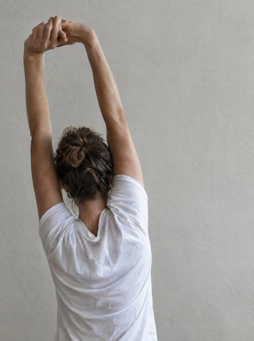 A person stretching their arms above their head by a concrete wall