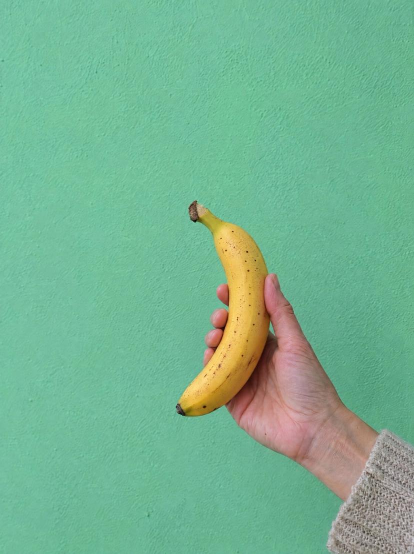 A hand holding a banana against a green wall