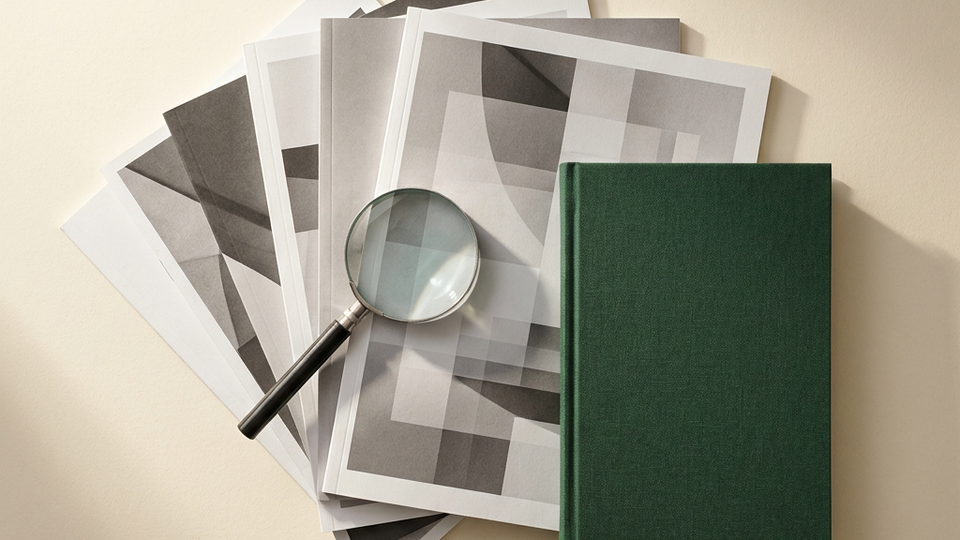 A magnifying glass and green notebook beside abstract research sheets.