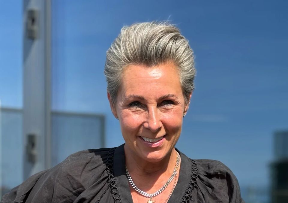Smilende kvinde med kort lyst hår foran en glasfacade