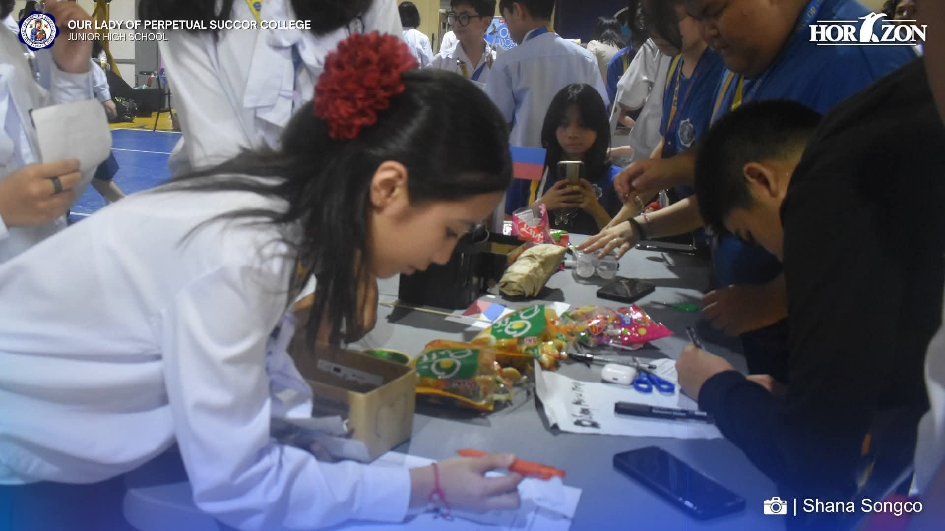 Junior High School students register for clubs at a booth during the OLOPSC Club Fair 2026 in the OLOPSC Gymnasium.