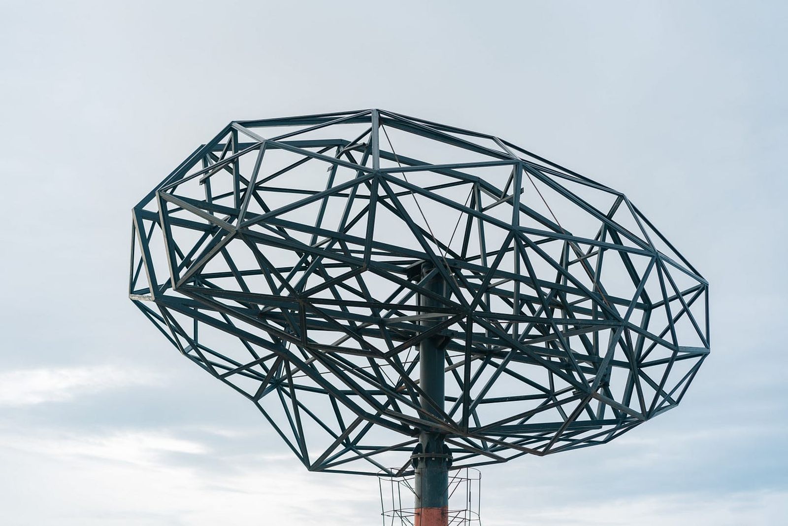 A brain-shaped steel wireframe structure against an overcast sky.