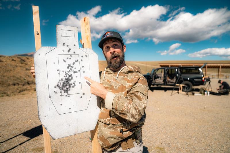 Shooter standing next to an IPSC paper target reviewing hits after a USPSA stage