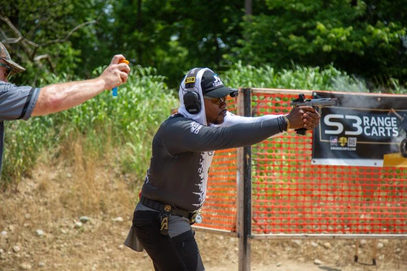 DJ Jenkins reloading mid-stage, extending his pistol toward a target behind the S3 Range Carts sign