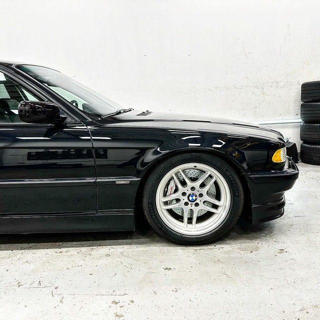 Close-up side view of a black BMW E38 7 Series front fender and M-Parallel wheel showing mirror-like paint finish after correction.
