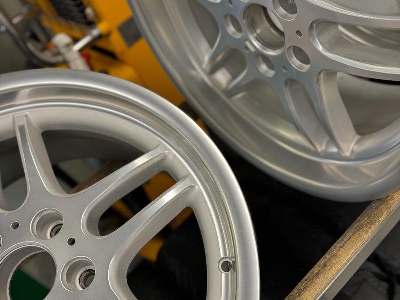 Two freshly refinished silver multi-spoke alloy wheels displayed in the shop, showing a clean satin finish.