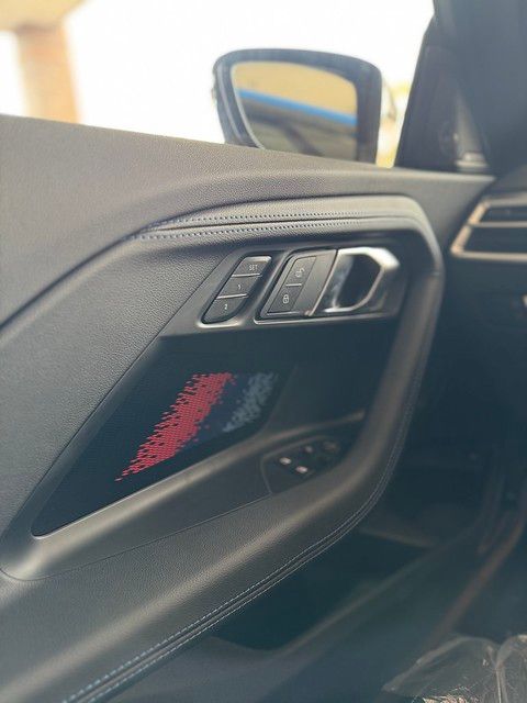 Close-up of a BMW driver's door panel showing leather trim, illuminated door handle with red ambient lighting, and memory seat controls.