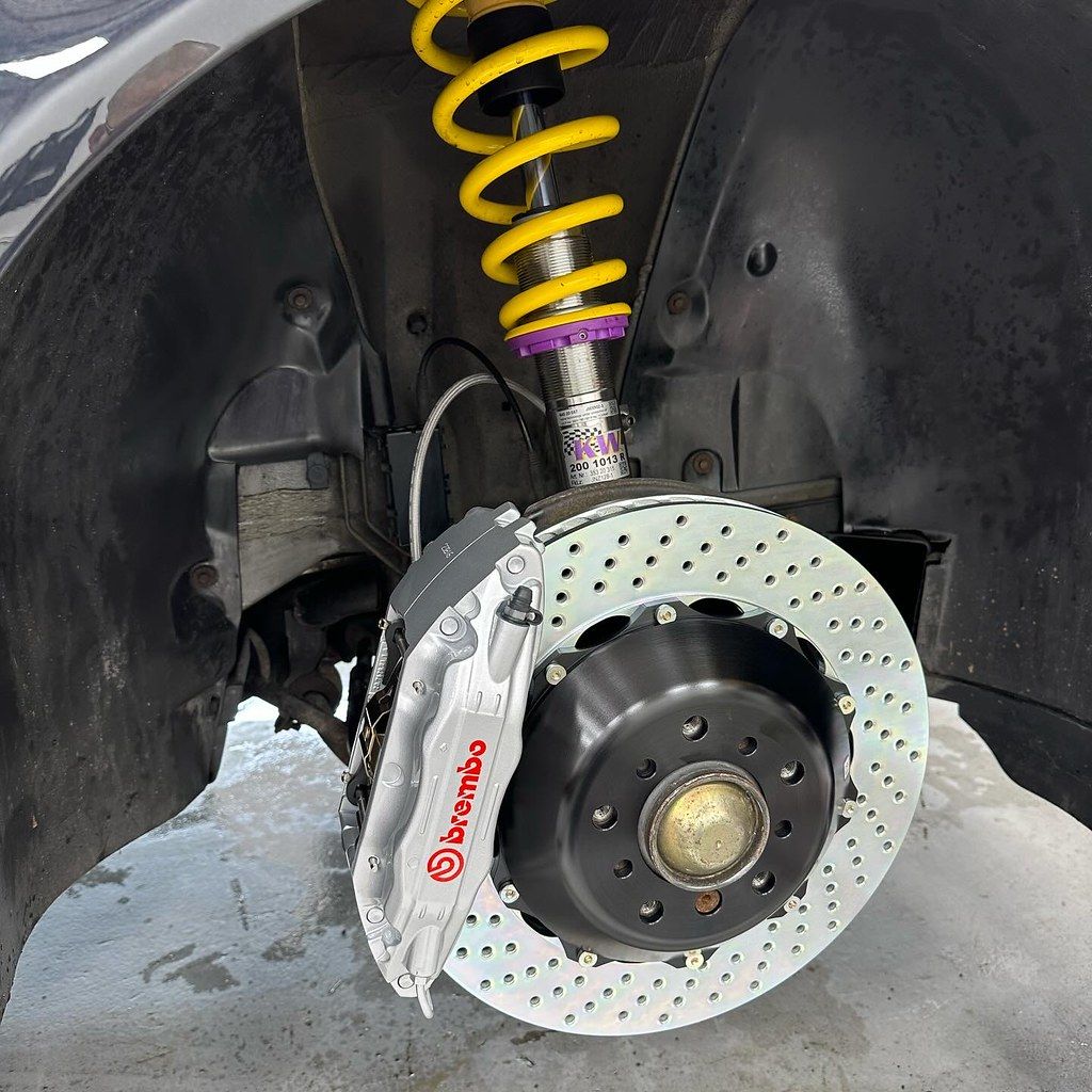 Close-up of a Brembo big brake kit and yellow KW coilover suspension installed on a BMW E38 with the wheel removed.