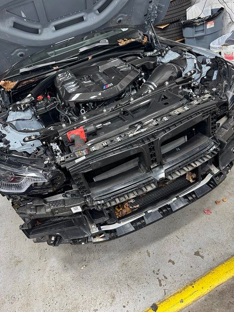 BMW M2 with front bumper and trim fully removed exposing the engine bay and radiator support, prepped for paint protection film installation.