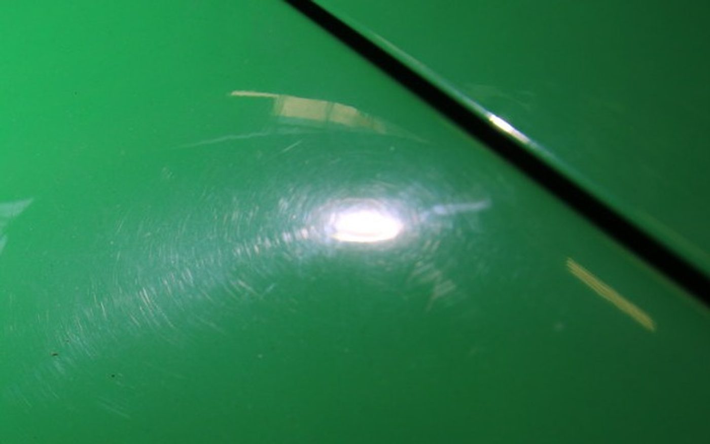 Green Porsche 964 fender under a handheld inspection light showing swirl marks ringing the reflection before paint correction