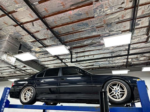 Black BMW E38 7 Series sedan elevated on a blue BendPak lift inside a well-lit shop, showing its full side profile and glossy paint.