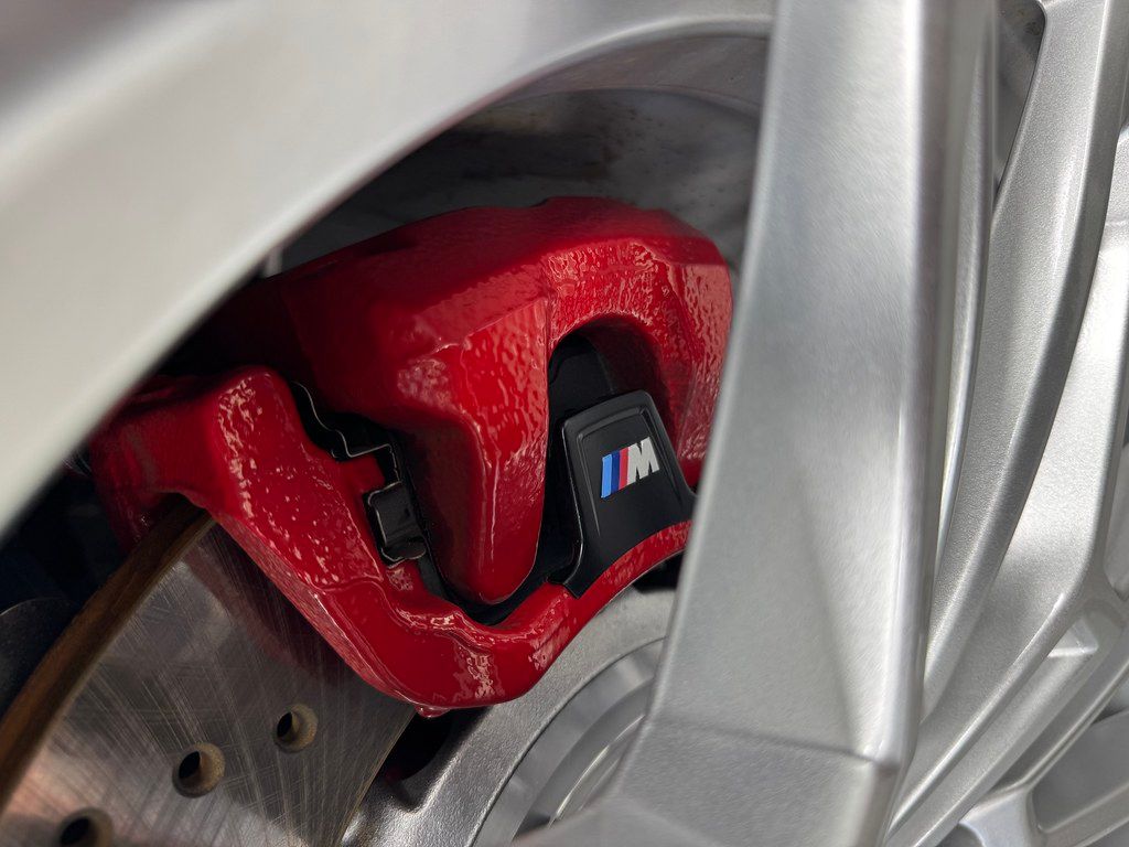 Close-up of a glossy red BMW M-branded brake caliper behind a silver multi-spoke wheel after thorough cleaning and detailing.