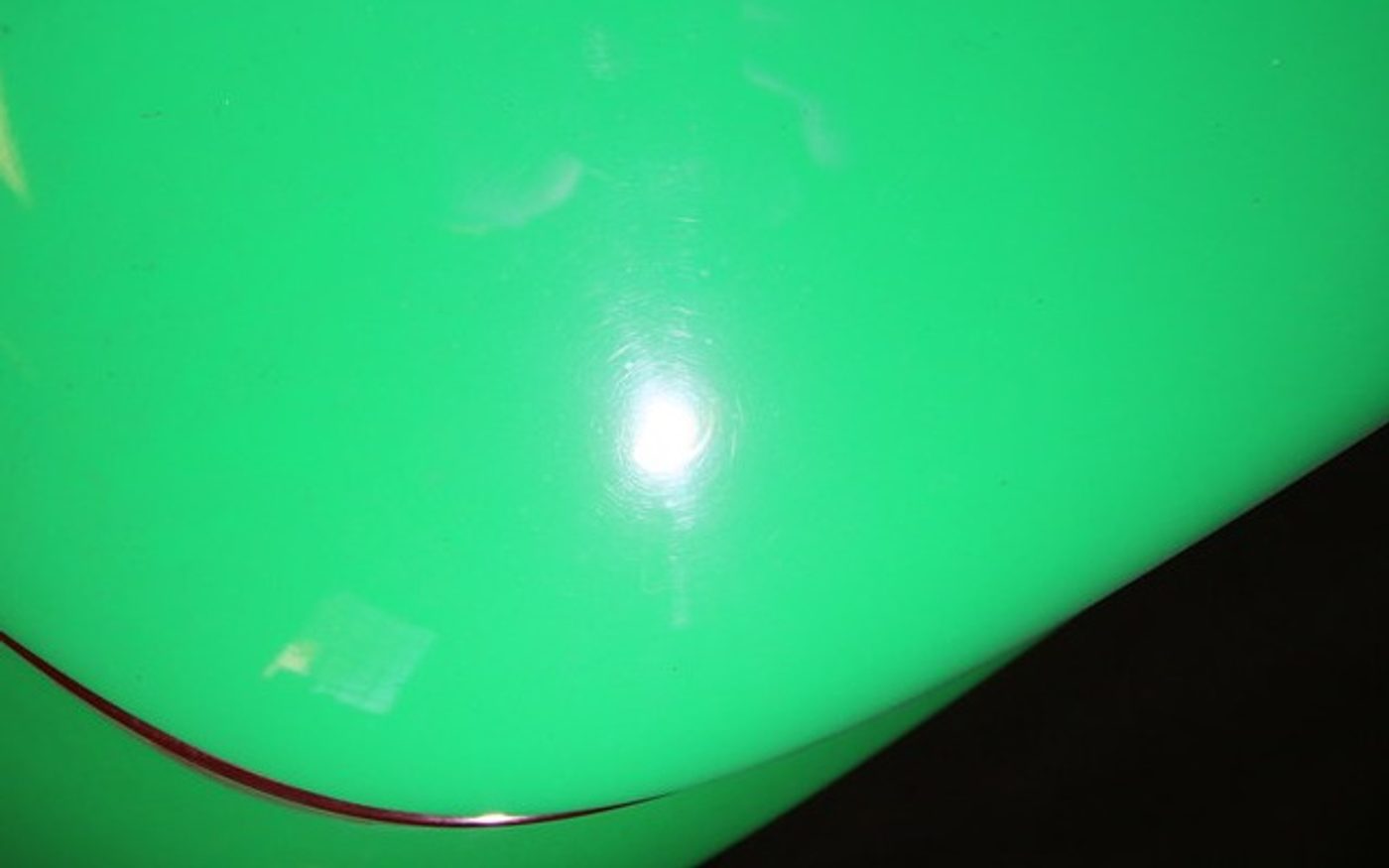 Green Porsche 964 hood under the same handheld inspection light after paint correction, reflection clean with no swirl marks