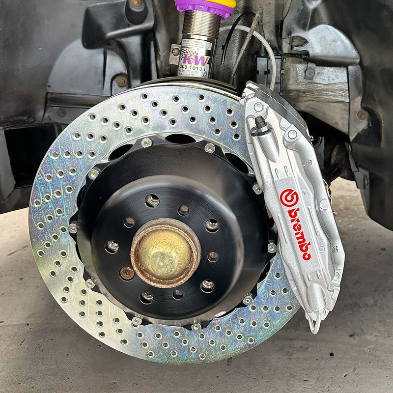 Close-up of a newly installed Brembo drilled brake rotor and silver caliper with KW coilover suspension visible in the wheel well.