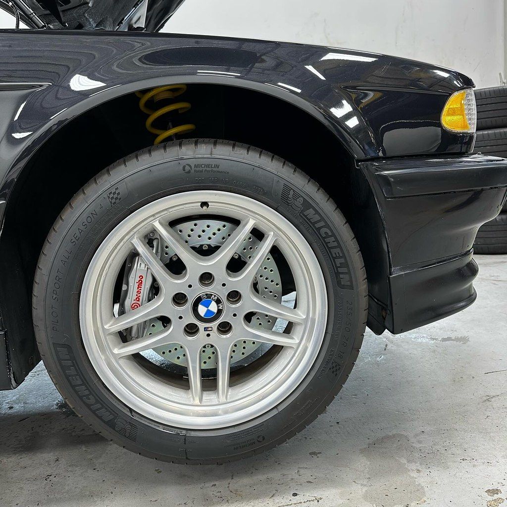 Close-up of a black BMW E38 front wheel showing M-Parallel style rim, Brembo brake caliper, and Michelin Pilot Sport tire.