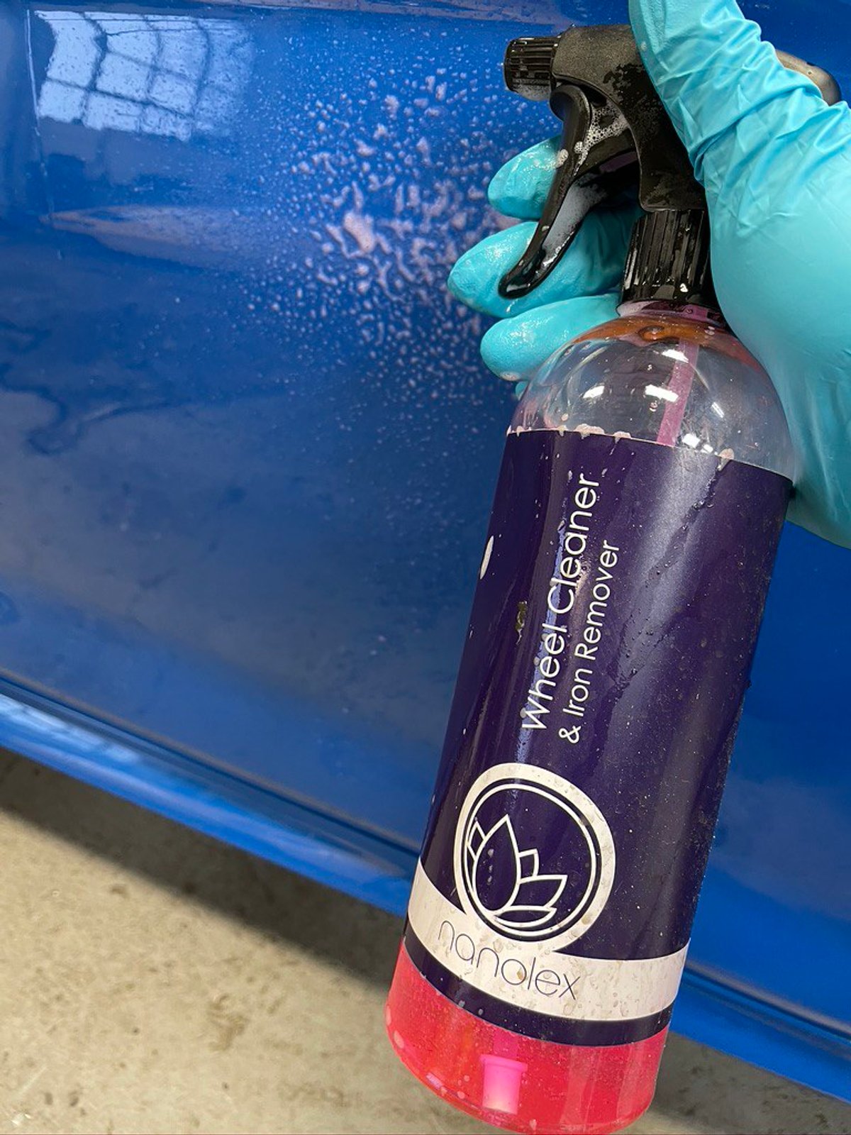 Nanolex Wheel Cleaner and Iron Remover held against the door of a blue BMW M2 CS, the spray turning red where it dissolves iron fallout