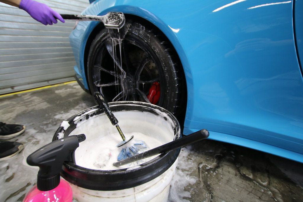 Wheel brush being rinsed over a wash bucket beside a Miami Blue Porsche 911 GT3