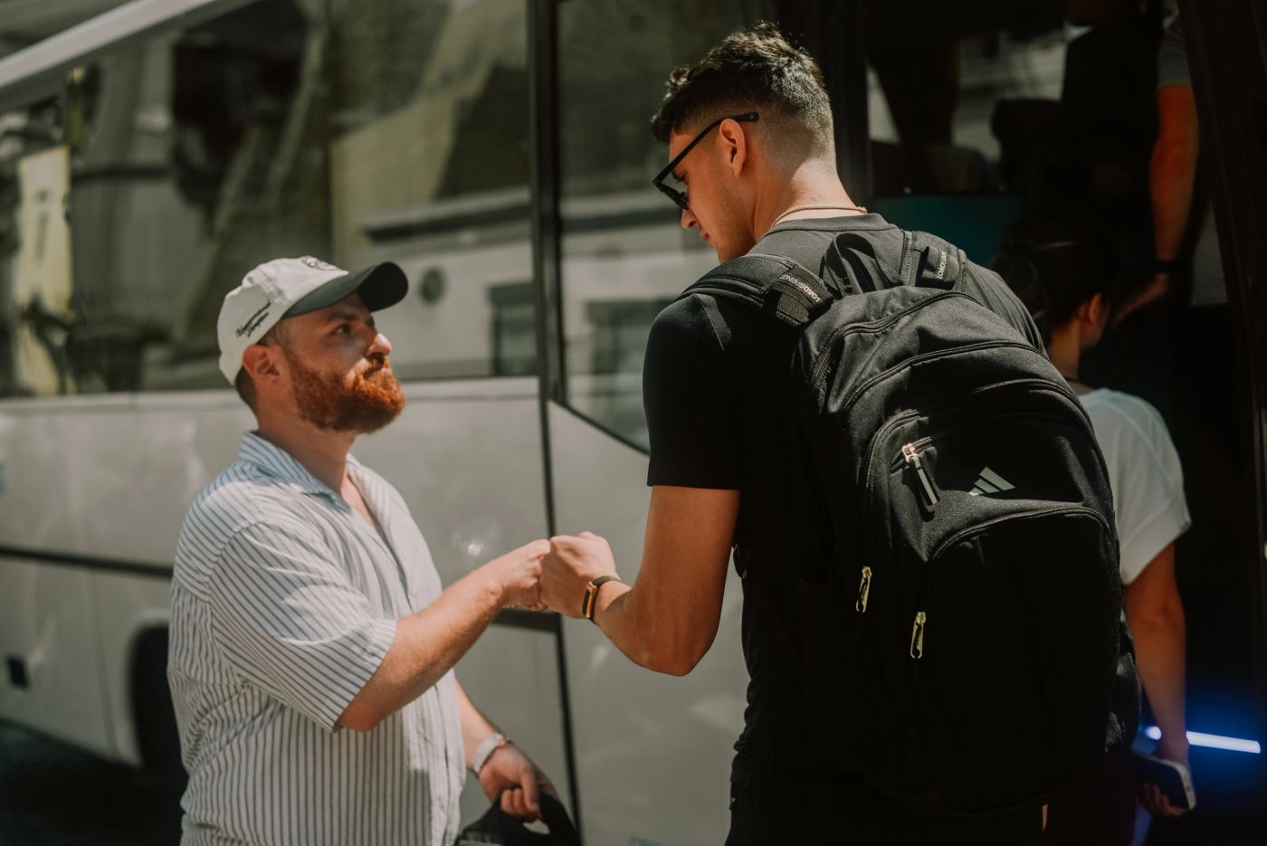 Tour guide greeting a client with a fist bump, next to the tour bus