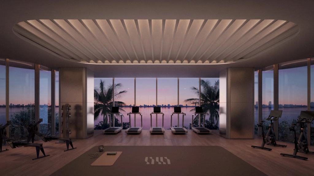 Fitness center with treadmills and bikes facing floor-to-ceiling windows and a bay sunset.