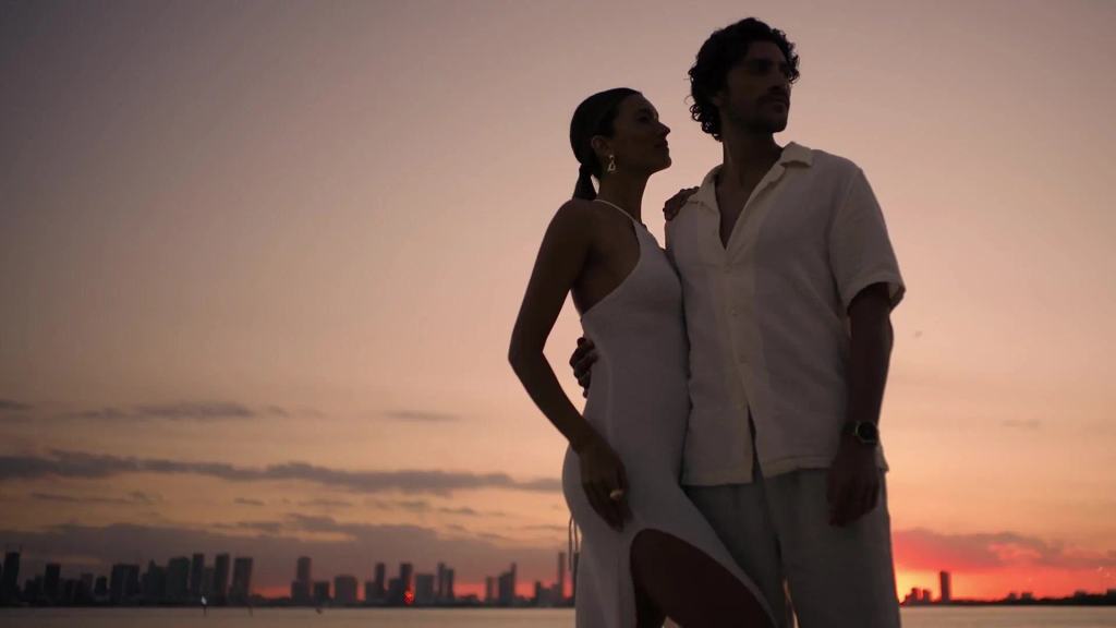 A couple in white standing together against a Miami skyline sunset over the bay.