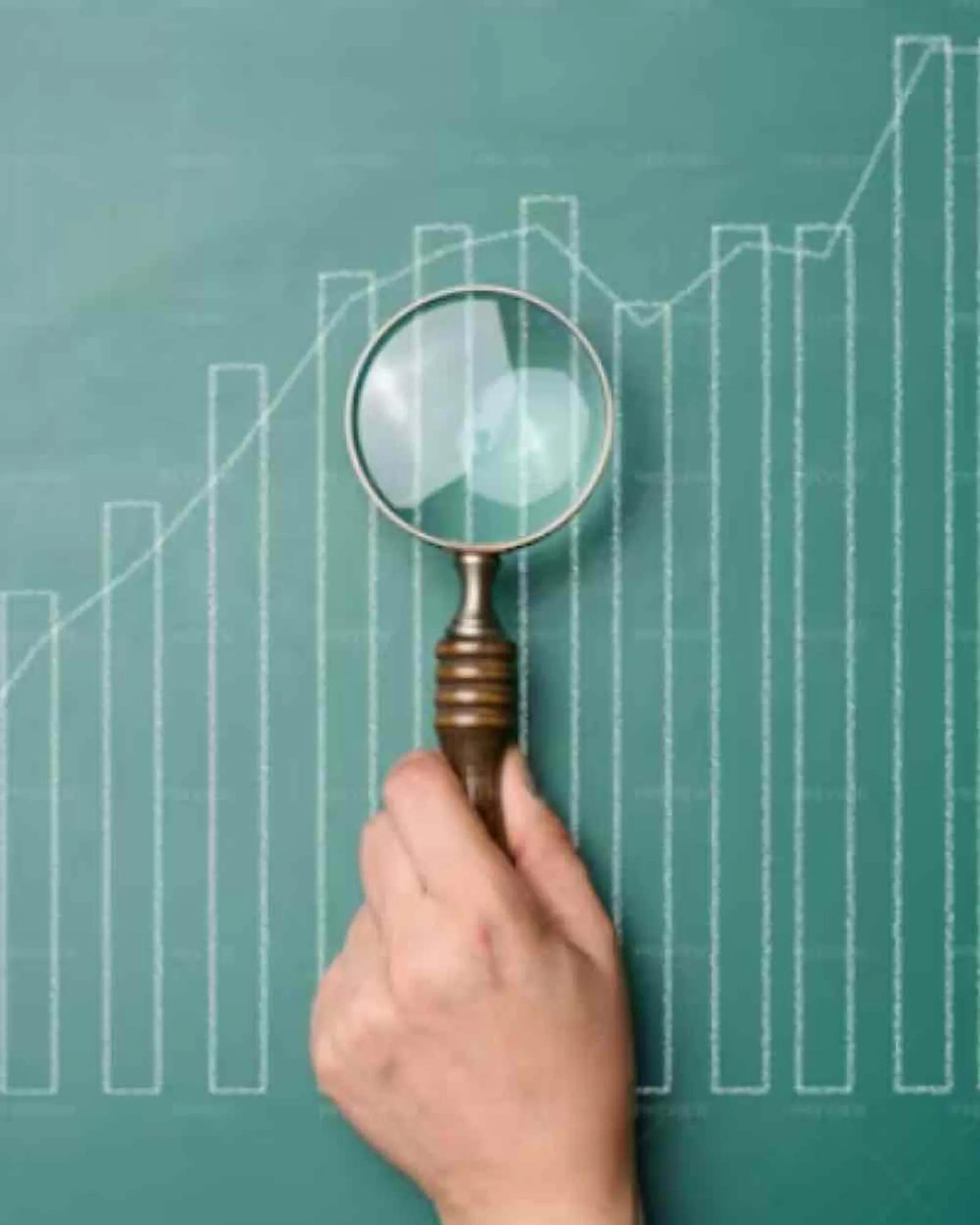 A hand holding a magnifying glass over a line graph.