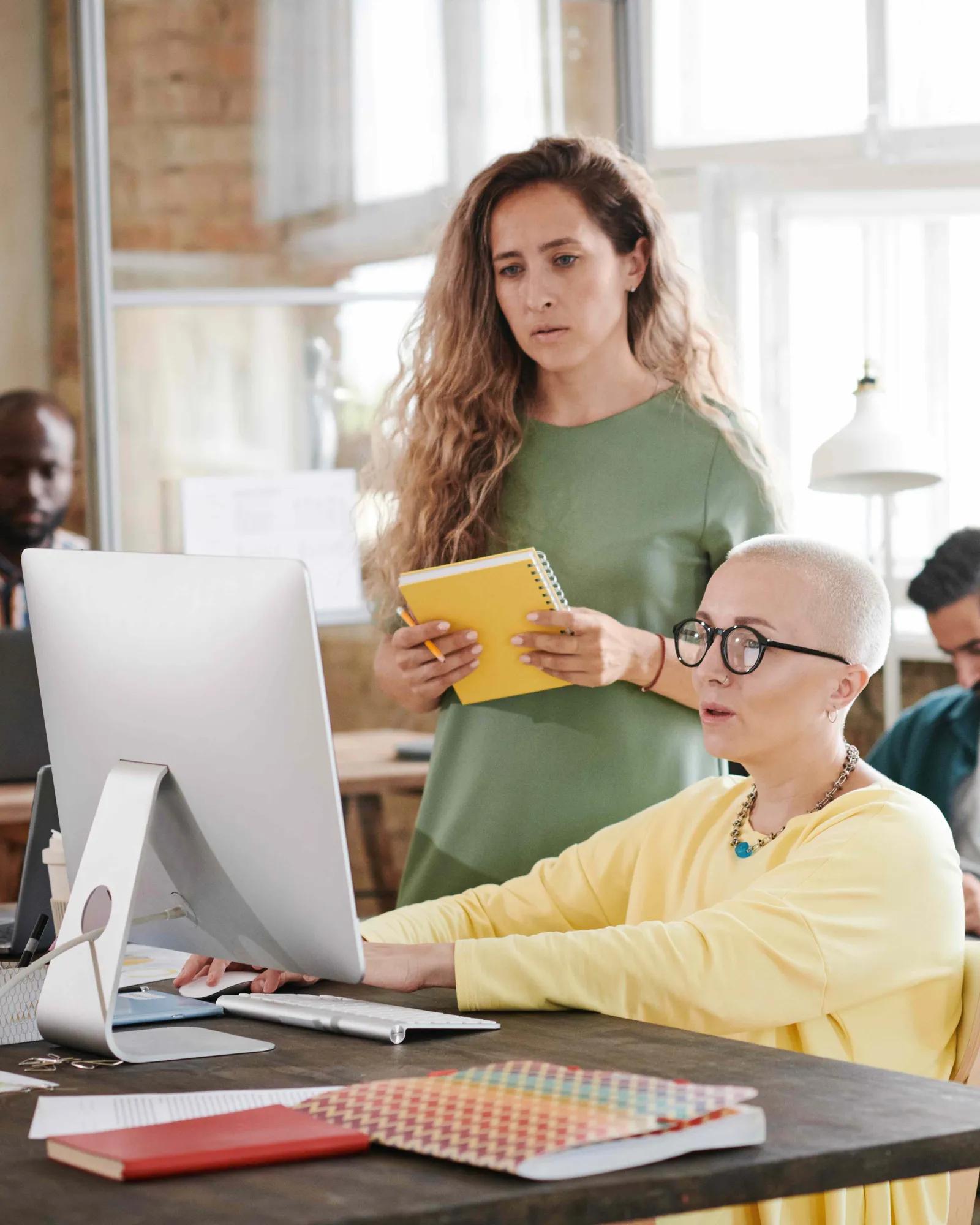 Two women looking at a computer, strategizing organic acquisition tactics.