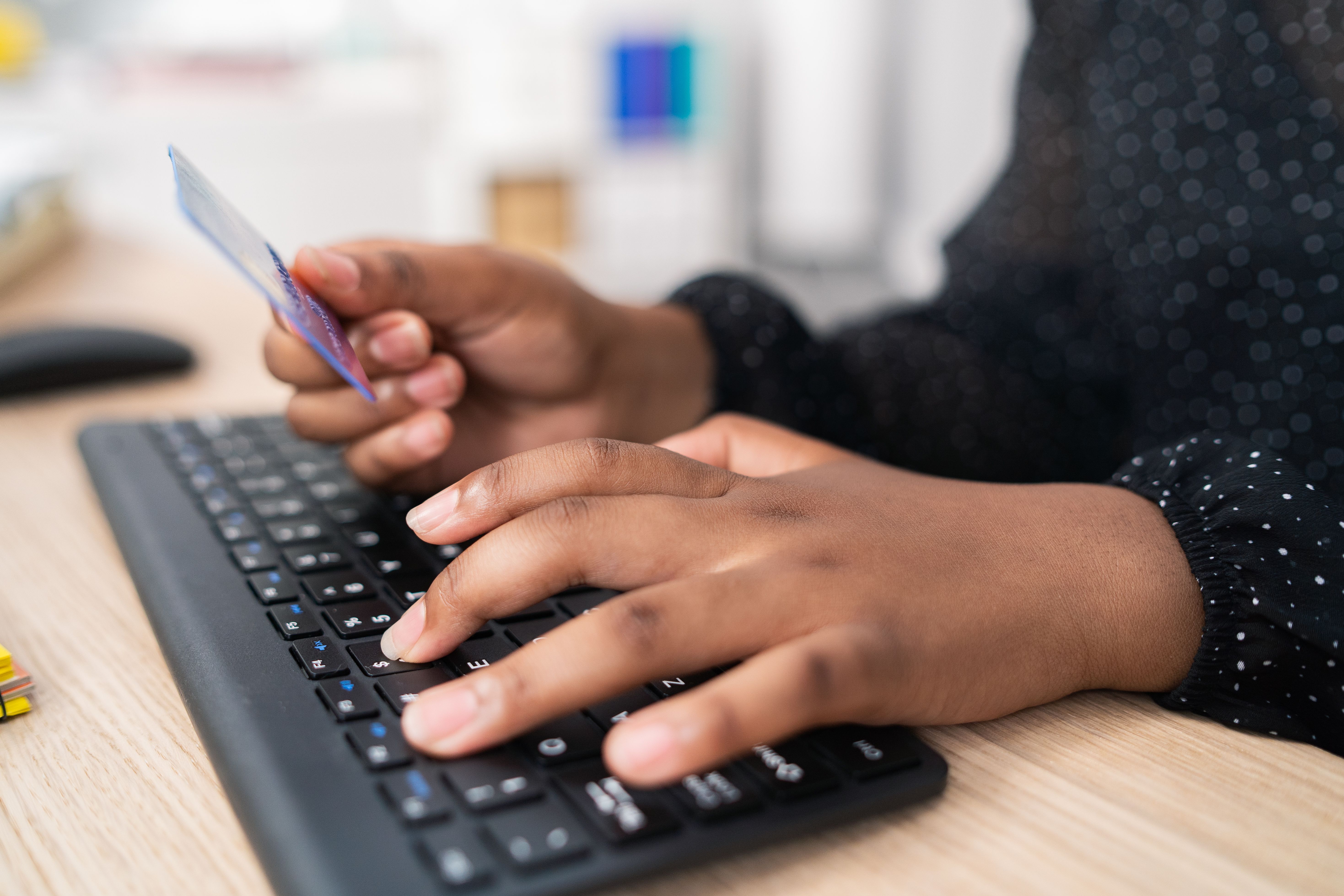 A person's hands holding a credit card while typing on a keyboard.