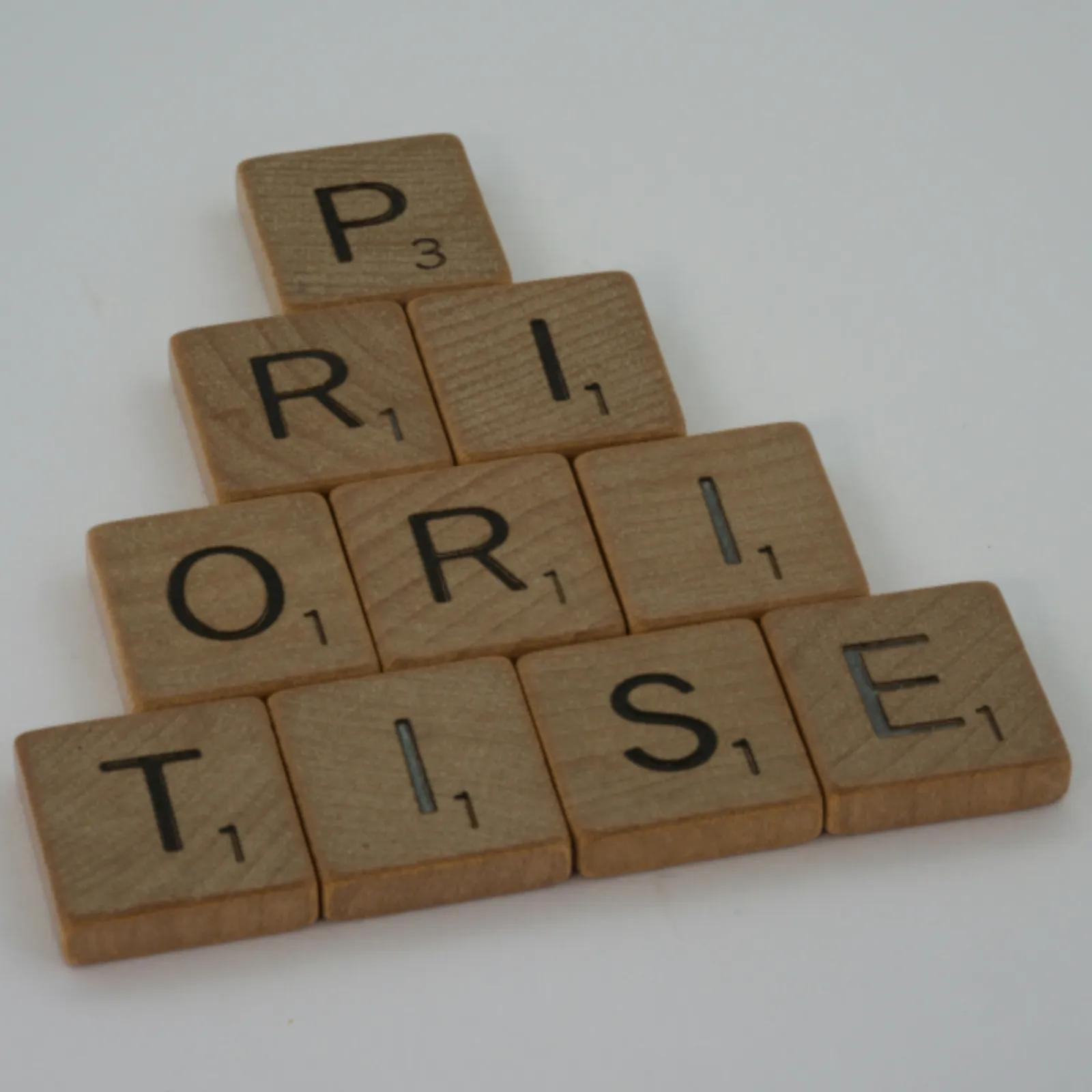 Wooden letter tiles stacked in a pyramid spell the word “PRIORITIES”