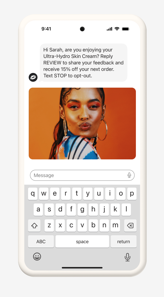 Smartphone displaying a text message requesting feedback for "Ultra-Hydro Skin Cream" with a 15% off offer, accompanied by a photo of a woman with vibrant makeup making a kissy face, and a virtual keyboard.