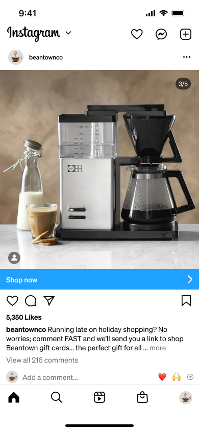 A silver and black coffee maker with a carafe of coffee, next to a glass of latte, a bottle of milk, and cookies on a marble countertop.