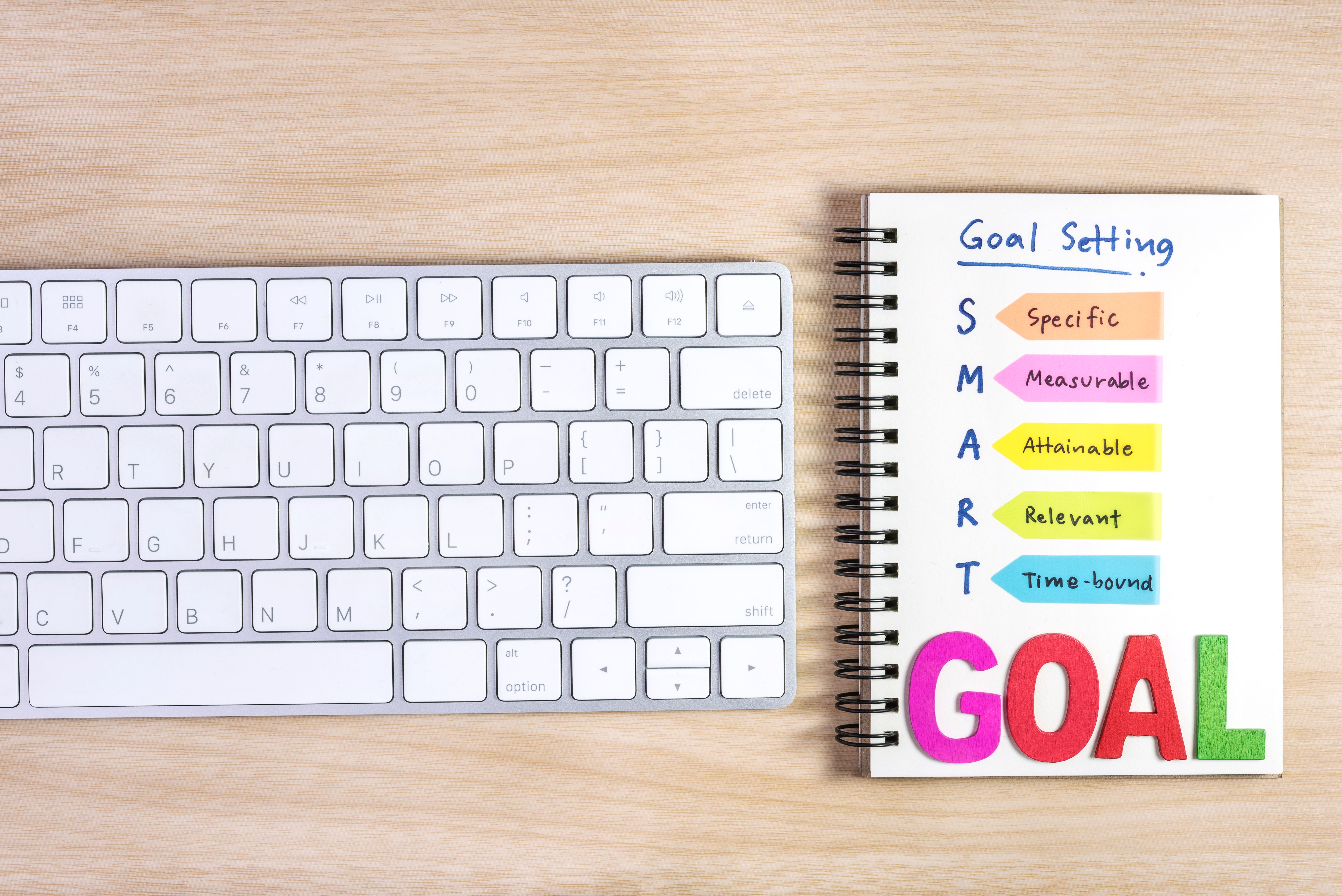 Notebook with SMART goal setting: Specific, Measurable, Attainable, Relevant, Time-bound, next to a keyboard.
